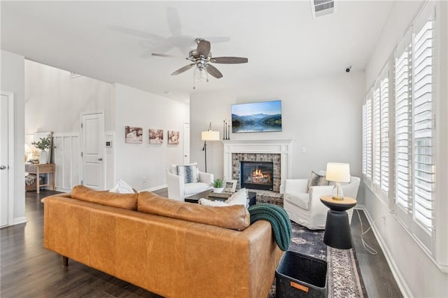 living room with visible vents, baseboards, ceiling fan, a glass covered fireplace, and dark wood-style flooring