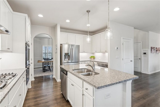 kitchen with a kitchen island with sink, a sink, stainless steel appliances, arched walkways, and decorative backsplash