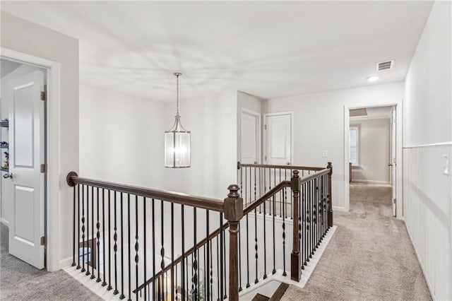 hallway with visible vents, an upstairs landing, light colored carpet, and a notable chandelier