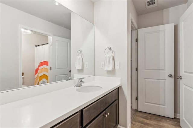 bathroom with vanity, toilet, wood finished floors, and visible vents