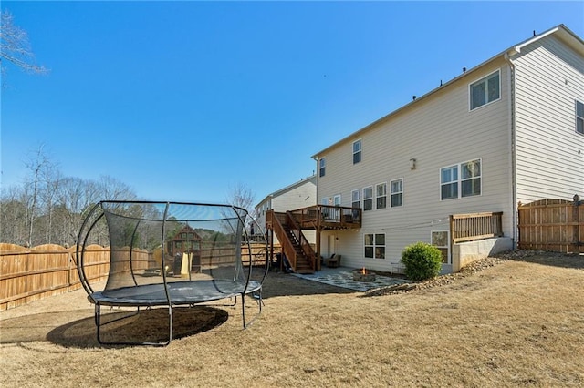 back of property featuring a deck, a trampoline, a fenced backyard, stairway, and a patio area