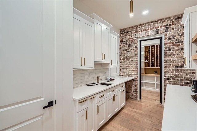 2625 Beverly Ln, Snellville, GA 30078 - kitchen featuring white cabinets, light wood-type flooring, light countertops, a sink, and brick wall