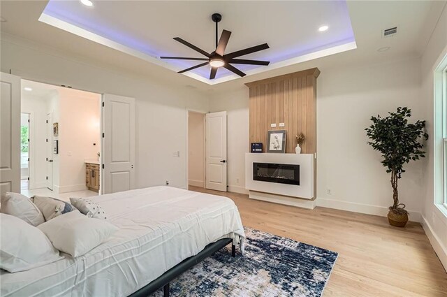 2625 Beverly Ln, Snellville, GA 30078 - bedroom featuring a tray ceiling, light wood-style flooring, recessed lighting, a glass covered fireplace, and baseboards