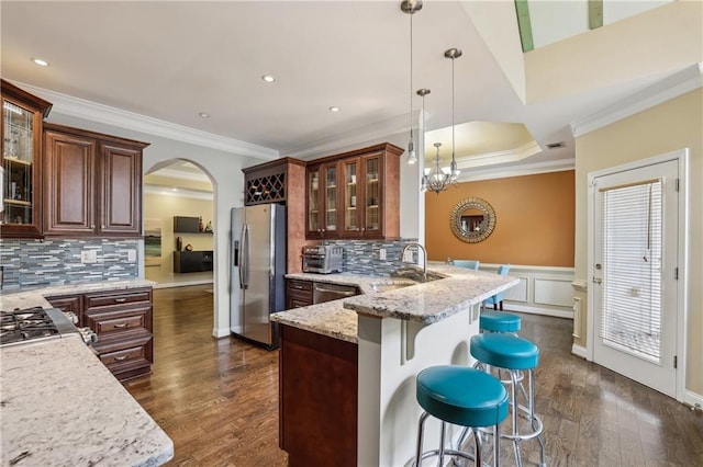 kitchen with arched walkways, stainless steel appliances, a peninsula, wainscoting, and a kitchen bar