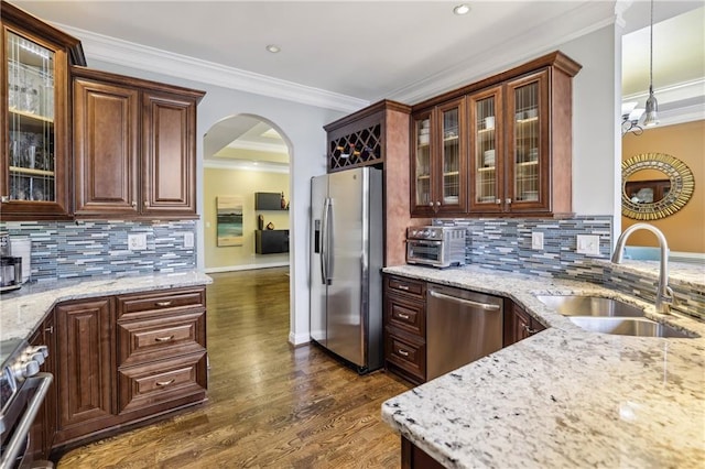 kitchen featuring dark wood-style floors, light stone counters, ornamental molding, stainless steel appliances, and a sink