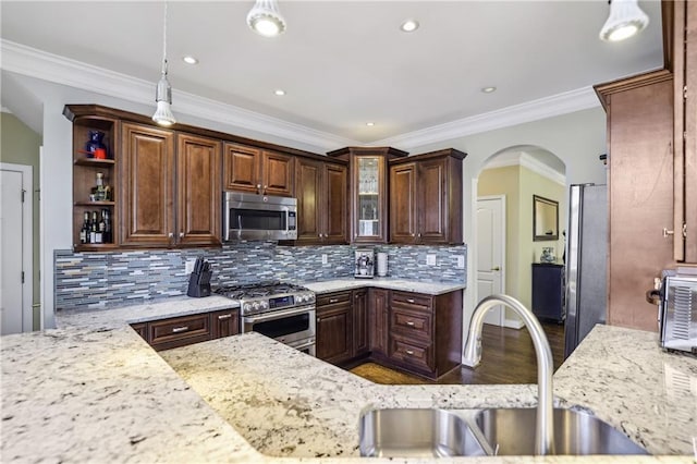 kitchen with arched walkways, tasteful backsplash, appliances with stainless steel finishes, a sink, and wood finished floors