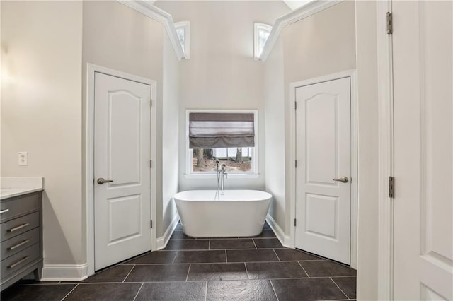 full bath featuring tile patterned flooring, a freestanding tub, vanity, and baseboards