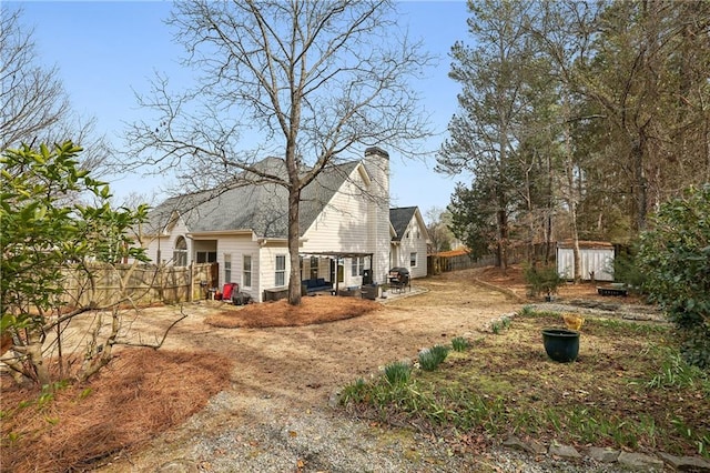 back of house with a patio, an outdoor structure, fence, a shed, and a chimney