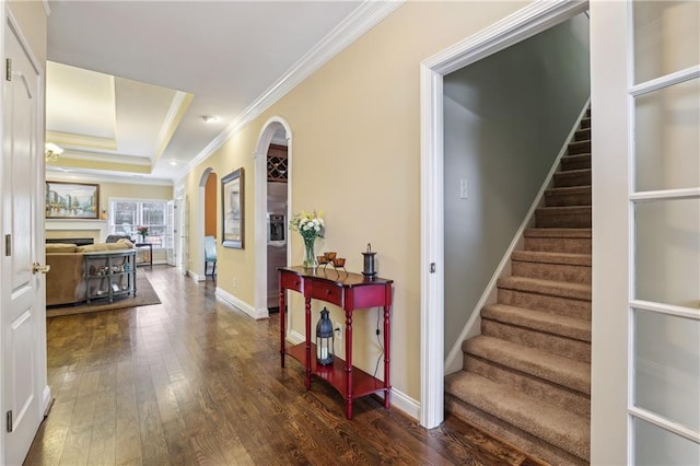 hall featuring arched walkways, dark wood-style floors, stairway, a tray ceiling, and crown molding