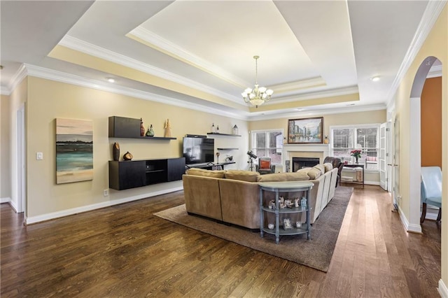 living area with dark wood-style floors, a tray ceiling, a fireplace, and a notable chandelier