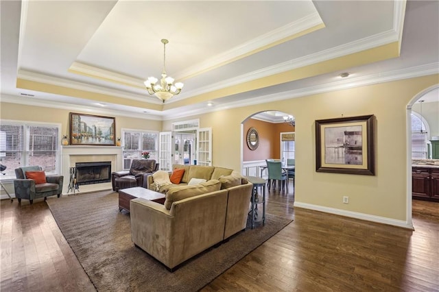 living area featuring a chandelier, a tray ceiling, dark wood finished floors, and arched walkways