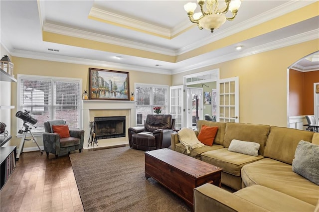 living room featuring arched walkways, a fireplace with raised hearth, hardwood / wood-style flooring, ornamental molding, and a tray ceiling