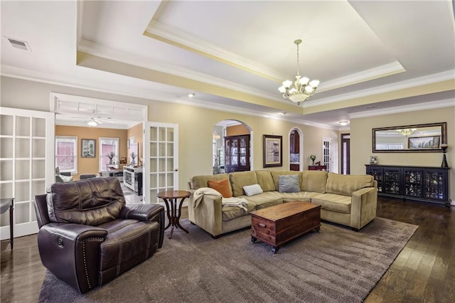 living area with arched walkways, a tray ceiling, plenty of natural light, and visible vents