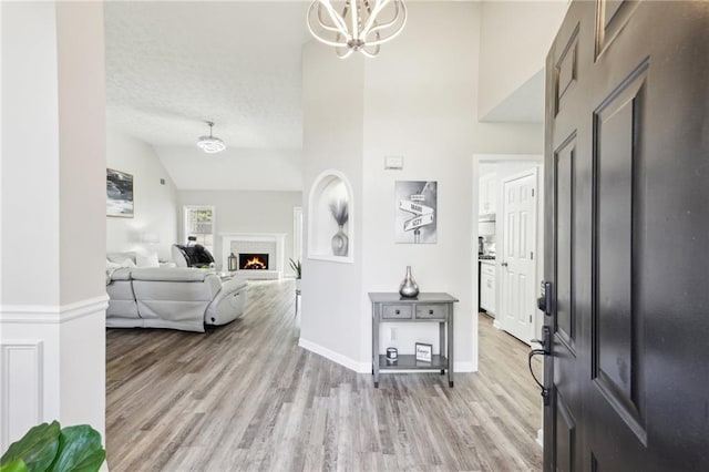 entrance foyer with light wood-style flooring, a textured ceiling, a warm lit fireplace, an inviting chandelier, and baseboards