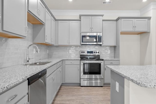 kitchen with appliances with stainless steel finishes, sink, gray cabinetry, crown molding, and light wood-type flooring