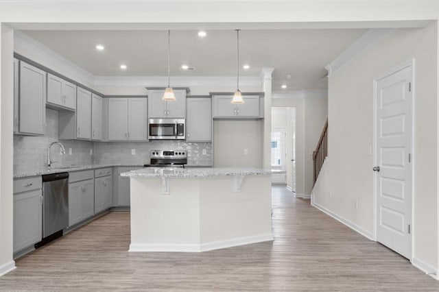 kitchen with stainless steel appliances, light stone countertops, a center island, and decorative light fixtures