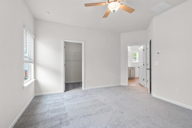 unfurnished bedroom featuring a walk in closet, light colored carpet, ceiling fan, ensuite bath, and a closet