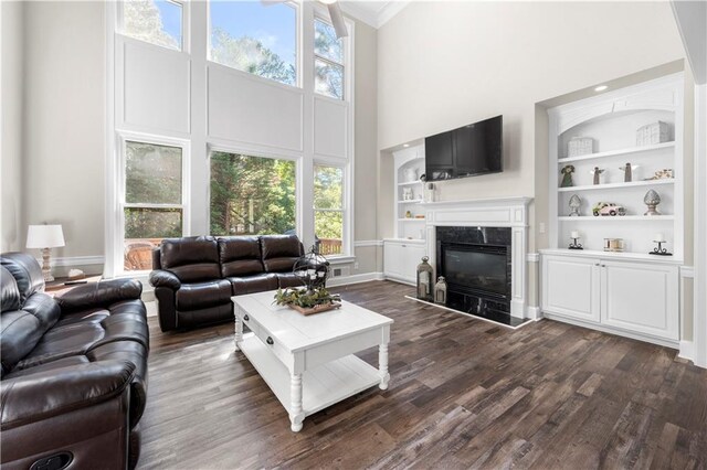 living room with built in shelves, a towering ceiling, dark wood-type flooring, and a healthy amount of sunlight