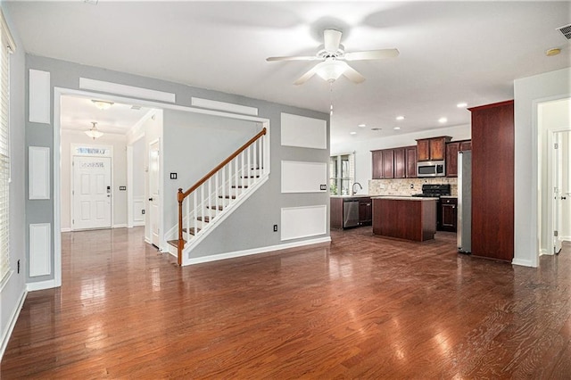 unfurnished living room featuring dark wood finished floors, stairway, a ceiling fan, and a sink