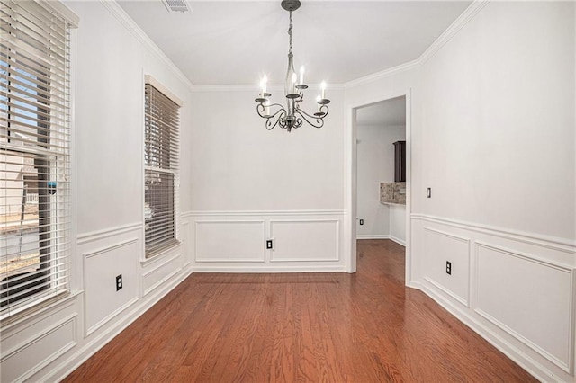 unfurnished dining area featuring a chandelier, visible vents, ornamental molding, and wood finished floors