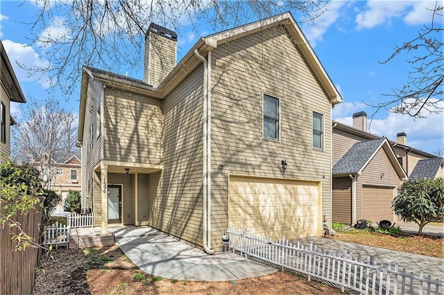 back of property featuring a fenced front yard, a porch, concrete driveway, a garage, and a chimney