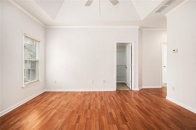 spare room with crown molding, a raised ceiling, baseboards, and wood finished floors