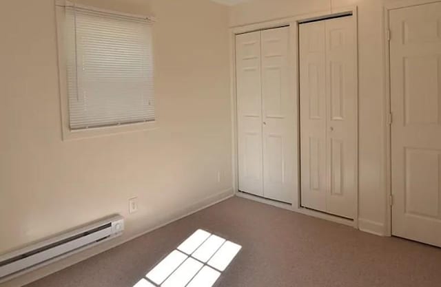 unfurnished bedroom featuring baseboards, baseboard heating, carpet flooring, and multiple closets