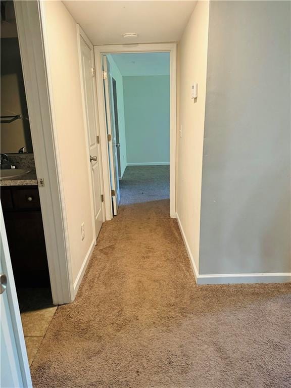 hall with baseboards, a sink, and light colored carpet