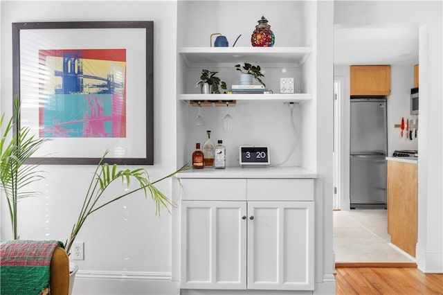 bar featuring light wood-type flooring, white cabinets, and stainless steel refrigerator