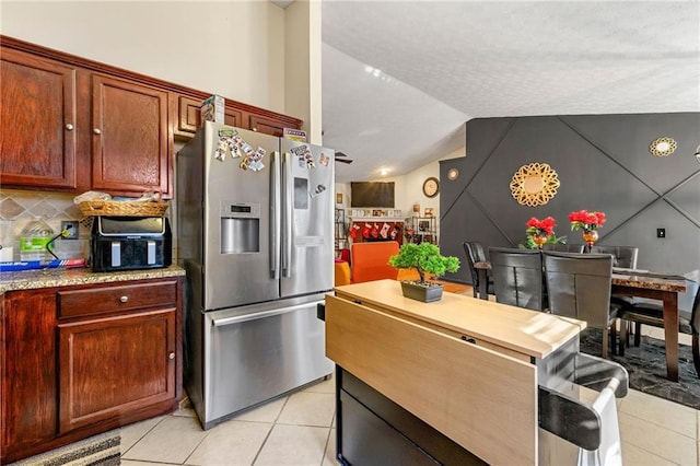 kitchen with stainless steel fridge, light tile patterned flooring, lofted ceiling, and tasteful backsplash