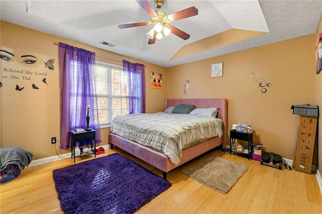 bedroom featuring wood finished floors, a ceiling fan, a textured ceiling, baseboards, and vaulted ceiling