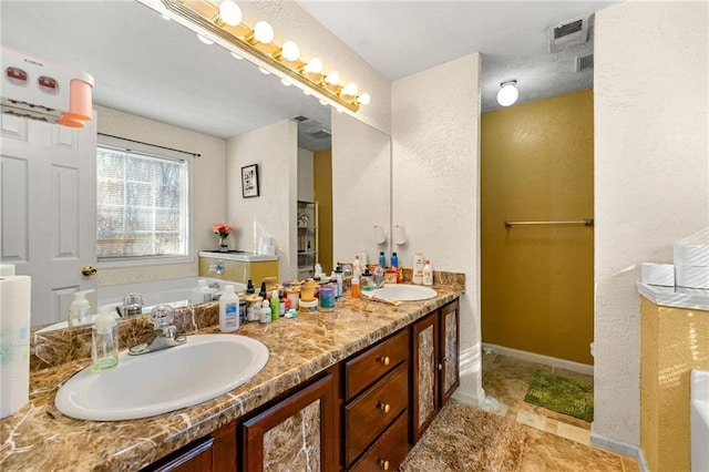 full bath featuring a garden tub, double vanity, a textured wall, and baseboards