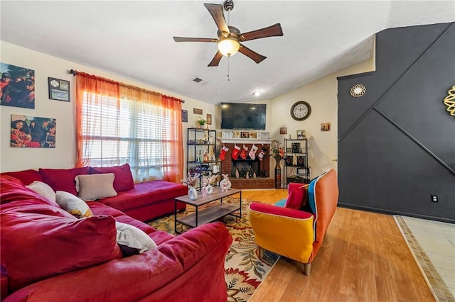 living room featuring ceiling fan, a fireplace, wood finished floors, and lofted ceiling