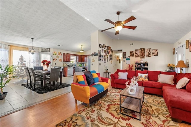 living area featuring light wood-style flooring, a ceiling fan, vaulted ceiling, and a textured ceiling