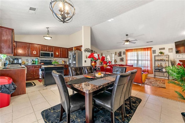 dining space with vaulted ceiling, light tile patterned floors, ceiling fan, and a chandelier