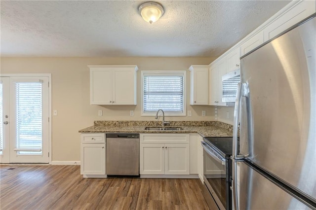 kitchen with a sink, appliances with stainless steel finishes, wood finished floors, and white cabinets