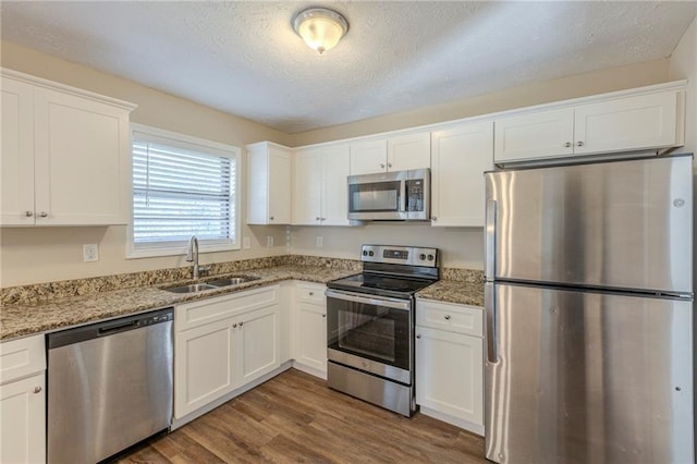 kitchen with light stone counters, dark wood-style flooring, a sink, white cabinets, and appliances with stainless steel finishes