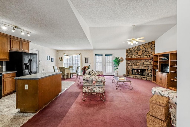 living area with carpet, lofted ceiling, a ceiling fan, a stone fireplace, and a textured ceiling