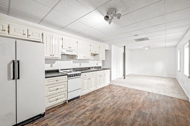 kitchen with white appliances, dark wood finished floors, dark countertops, a paneled ceiling, and under cabinet range hood