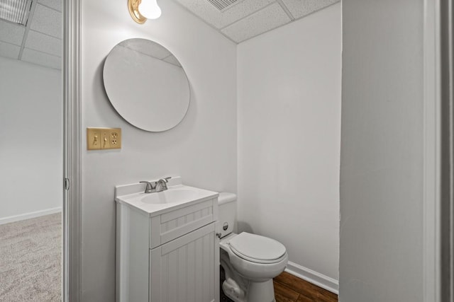 half bath with toilet, baseboards, a drop ceiling, and vanity