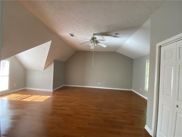 bonus room featuring vaulted ceiling, a textured ceiling, dark hardwood / wood-style flooring, and ceiling fan