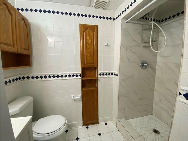 bathroom with vanity, toilet, tile walls, and tiled shower