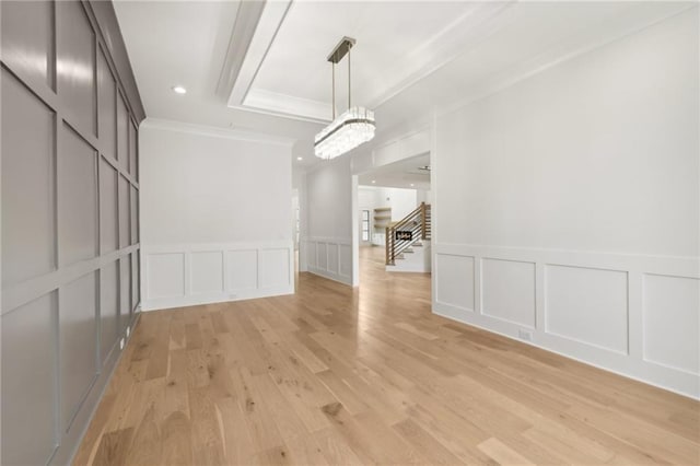 unfurnished dining area featuring crown molding, stairway, light wood-style floors, a decorative wall, and a raised ceiling