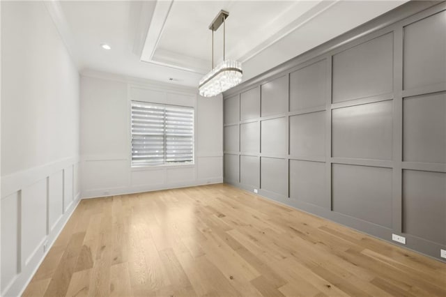 unfurnished dining area featuring a chandelier, a tray ceiling, ornamental molding, light wood-style flooring, and a decorative wall