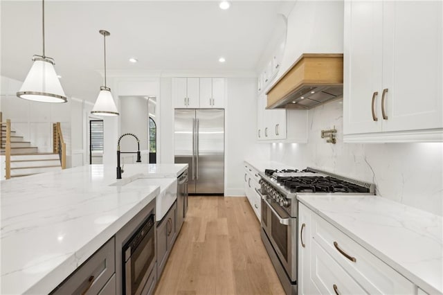 kitchen featuring custom exhaust hood, white cabinets, built in appliances, decorative light fixtures, and backsplash