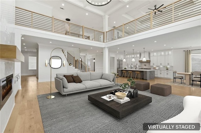 living room with stairway, ornate columns, light wood-style floors, a towering ceiling, and a tiled fireplace