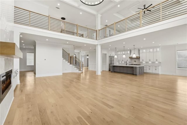 living area with ceiling fan, decorative columns, light wood-style flooring, a fireplace, and a towering ceiling