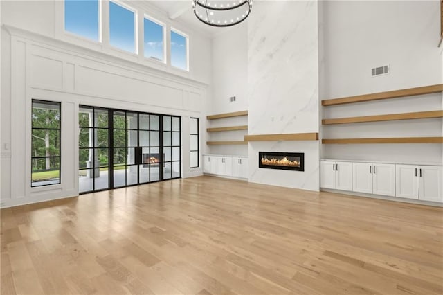 unfurnished living room featuring visible vents, light wood-type flooring, a fireplace, an inviting chandelier, and a towering ceiling