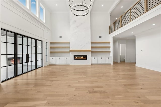 unfurnished living room with a towering ceiling, light wood-style flooring, a high end fireplace, and ornamental molding