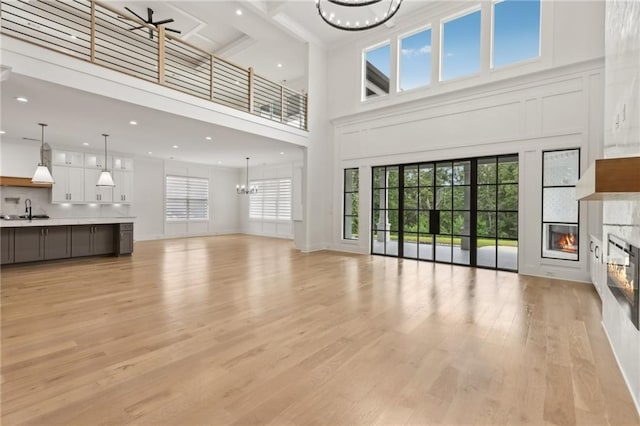 living area with recessed lighting, light wood-style flooring, ceiling fan with notable chandelier, a towering ceiling, and a glass covered fireplace